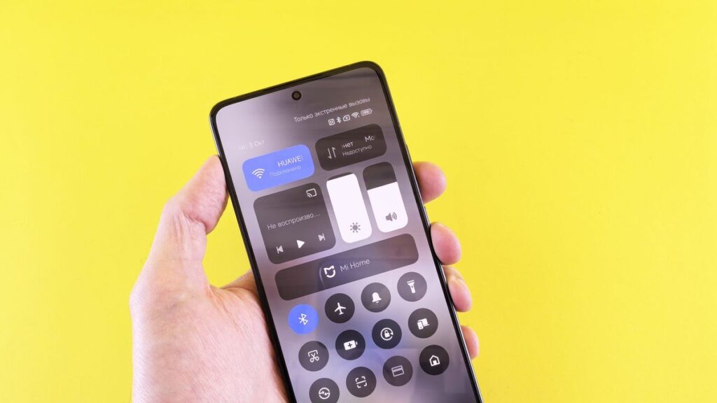 Close-up of a hand holding a smartphone against a vibrant yellow backdrop.
