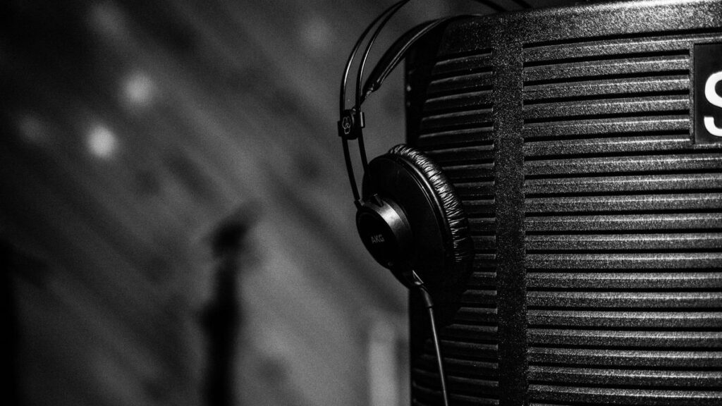 Close-up grayscale image of studio headphones hung on acoustic panel, depicting a professional music production environment.