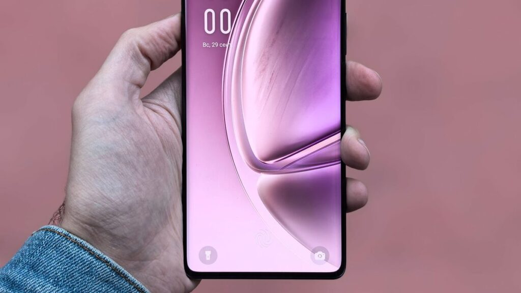 A person holding a sleek, modern smartphone with a purple screen against a plain background.