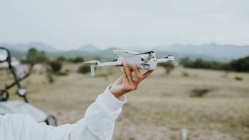 A person holding a drone against a mountain backdrop, ready for flight.