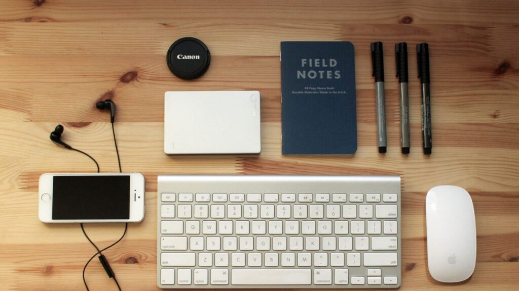 Top view of a modern desk setup featuring electronics, stationery, and gadgets on a wooden surface.
