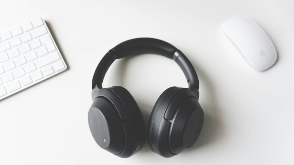 black wireless headphones between Apple Keyboard and Apple Magic Mouse on white surface