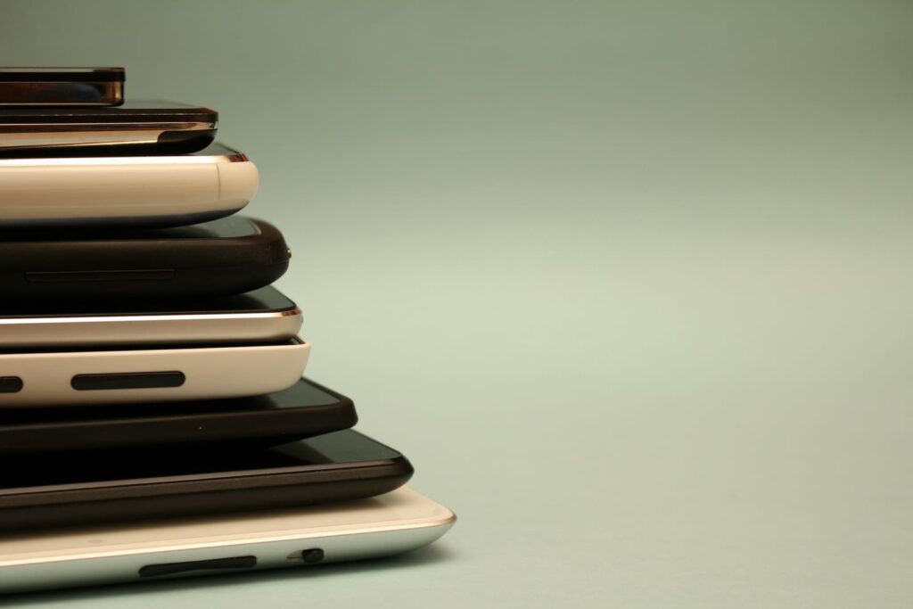 A stack of older smartphones in different colors seen from the side against a plain green background