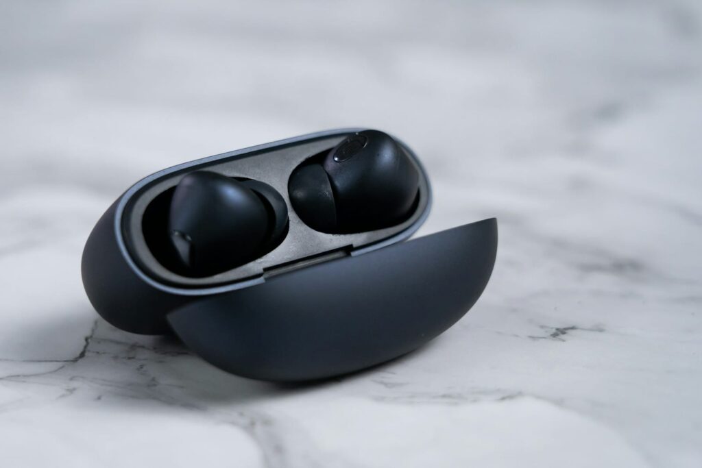 A pair of black wireless earbuds in an open charging case on a white marble surface